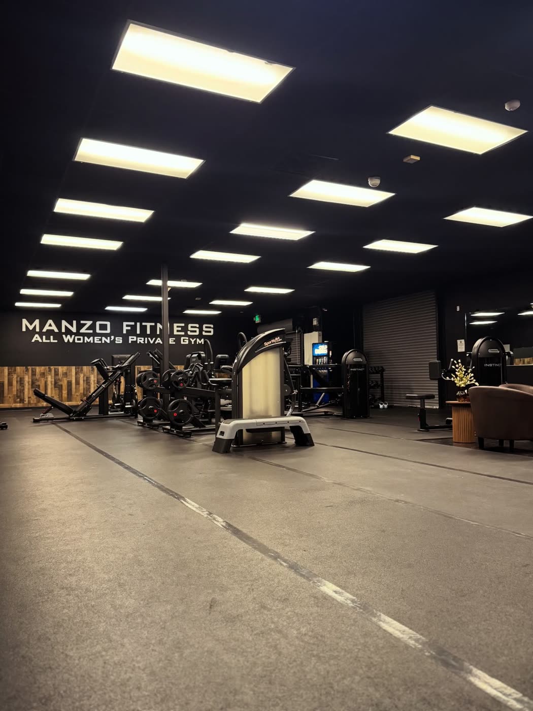 Wide view of the Fresno gym floor with strength machines under the Manzo Fitness wall sign